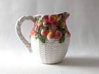 Decorative ceramic pitcher with fruit design on a plain background