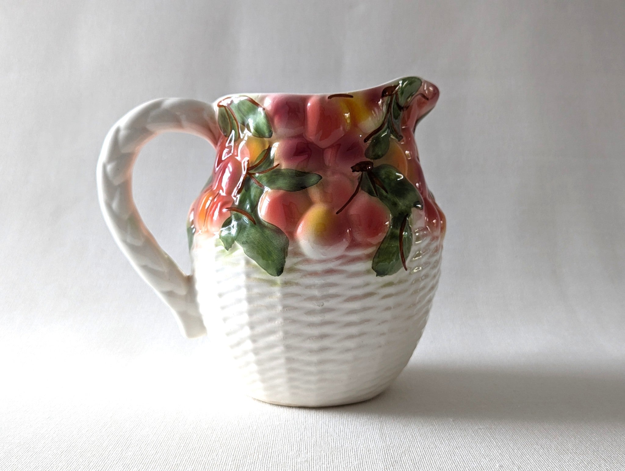 Decorative ceramic pitcher with fruit design on a plain background