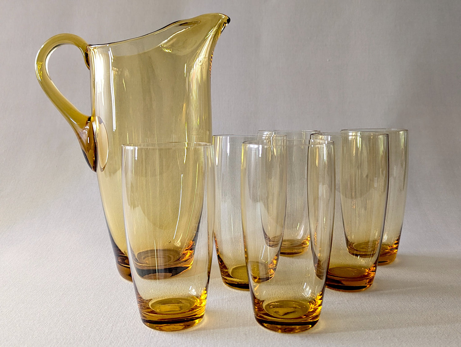 Set of amber glass pitcher and tumblers on a light gray background