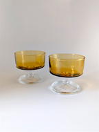 Two amber glass dessert bowls with clear stands on a white background
